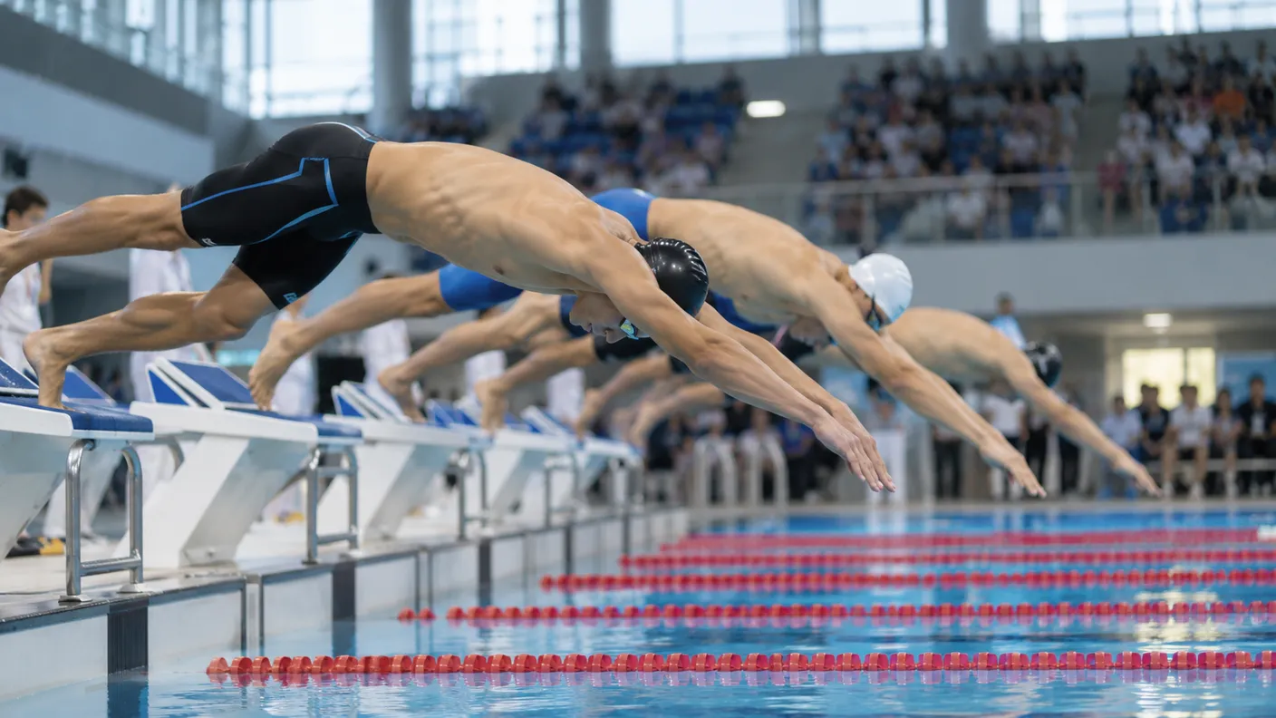 Swimmers diving off the starting blocks at an indoor meet